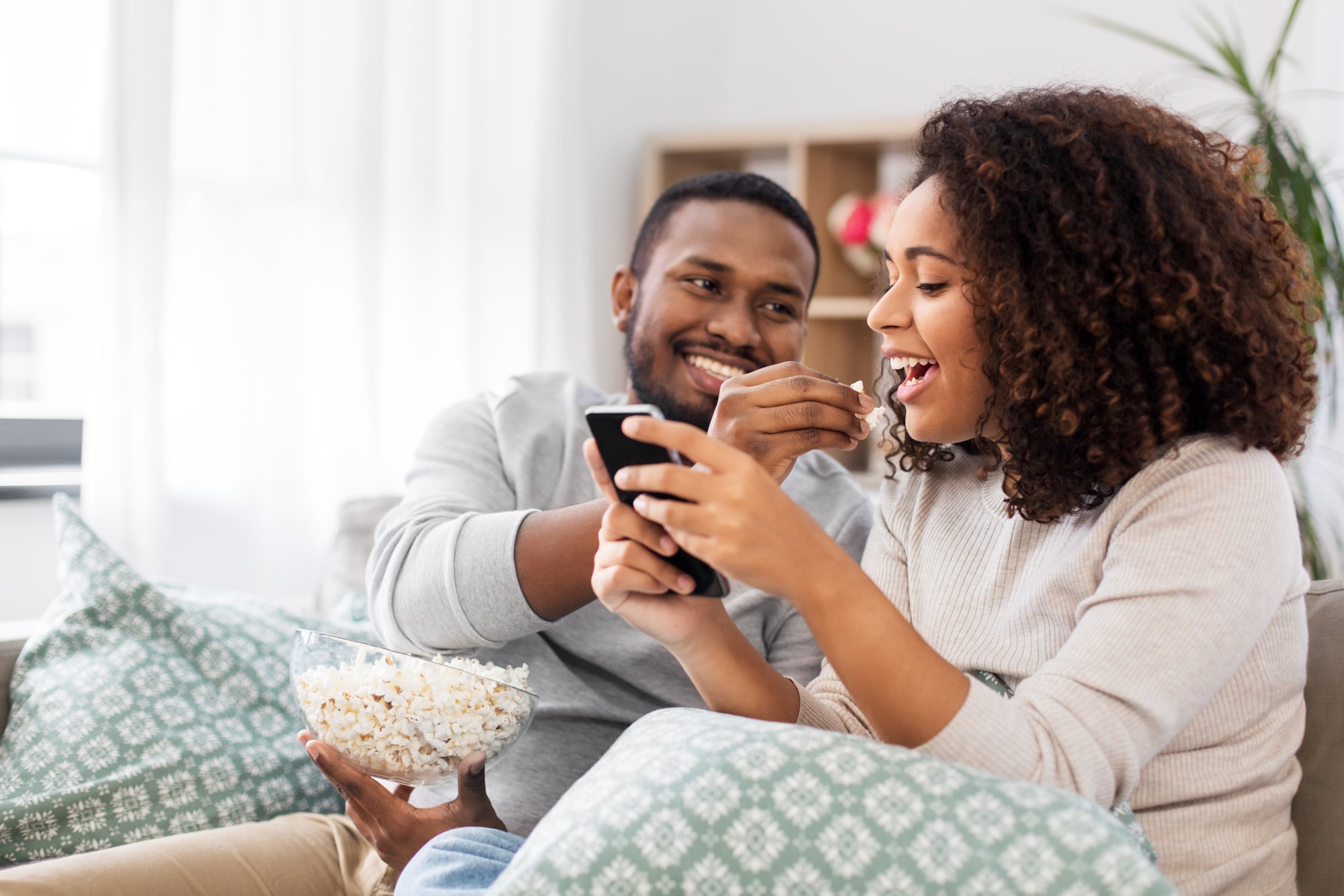 people and leisure concept - african american couple with popcorn and smartphone at home